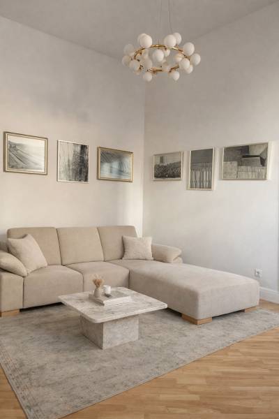 Obývací pokoj v 3-pokojovém bytě s béžovou sedačkou, stolkem, obrazy a podlahou s dřevěným dekorem.