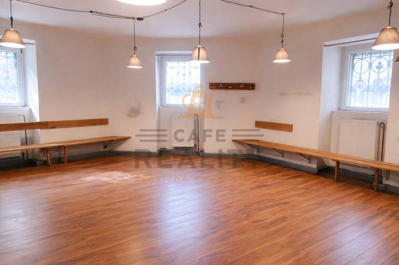 Obchodní prostory se stěnami, lavicemi a podlahou s dřevěným dekorem, osvětlené závěsnými lampami.