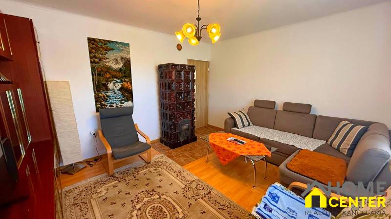 Obývací pokoj v rodinném domě s pohovkou, křeslem, kachlovými kamny a obrazem přírody.