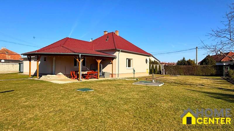 Rodinný dům v Zemianské Olči s červenou střechou a dřevěným přístřeškem, travnatá zahrada.