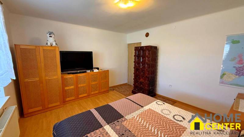 Pokoj v rodinném domě s televizí, skříní, kachlovými kamny a podlahou s dřevěným dekorem.