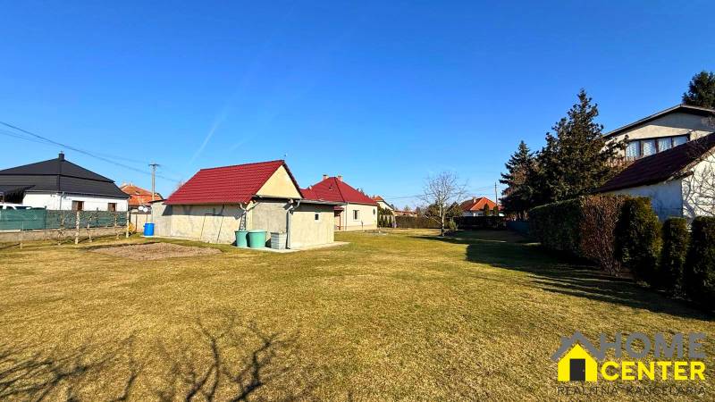 Travnatý pozemek u rodinného domu v Zemianské Olči s několika domy a keři.