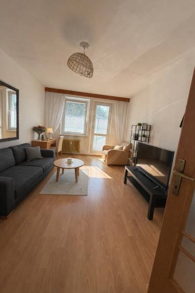 Obývací pokoj v 3-pokojovém bytě s podlahou s dřevěným dekorem a pohodlným nábytkem.