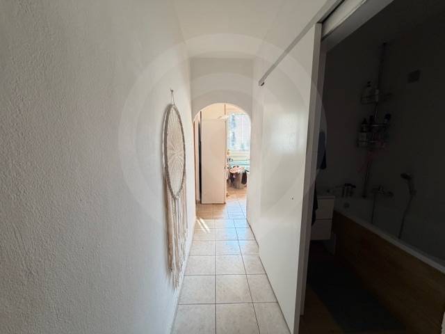 Chodba s dlažbou v 3-pokojovém bytě s dekorací na stěně a pohledem do koupelny.