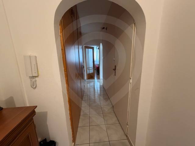 Chodba se světlou dlažbou, obloukovým průchodem a skříní v 3-pokojovém bytě.