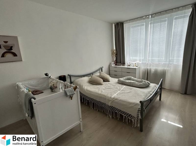 Ložnice v 2-pokojovém bytě s postýlkou, postelí a komodou, podlaha s dřevěným dekorem.