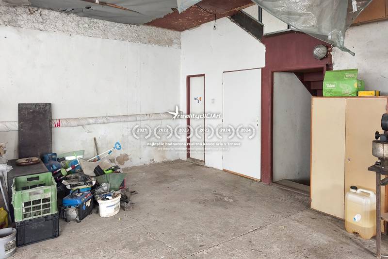 Garáž v rodinném domě, uložené nářadí, betonová podlaha, schody a bílý nábytek.