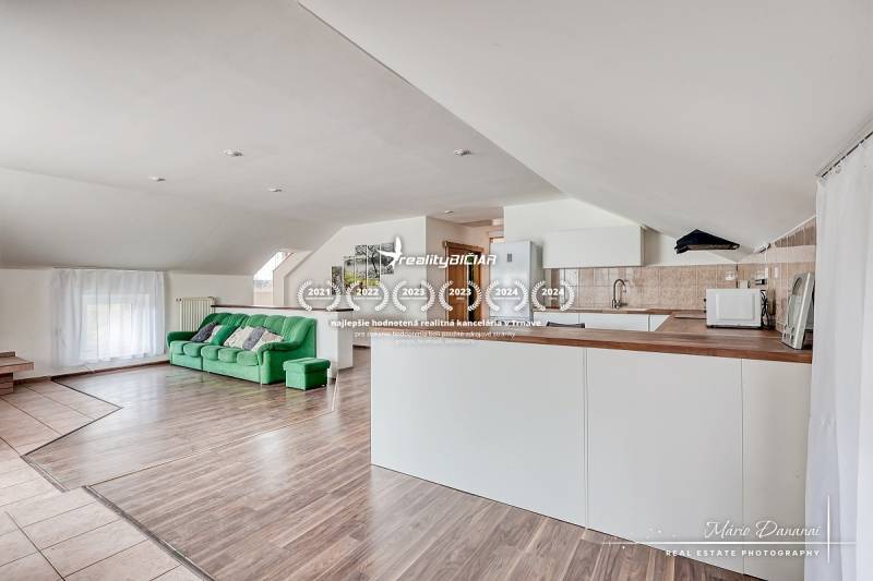 Obývací pokoj s kuchyní, zelená sedačka, bílý nábytek, podlaha s dřevěným dekorem.