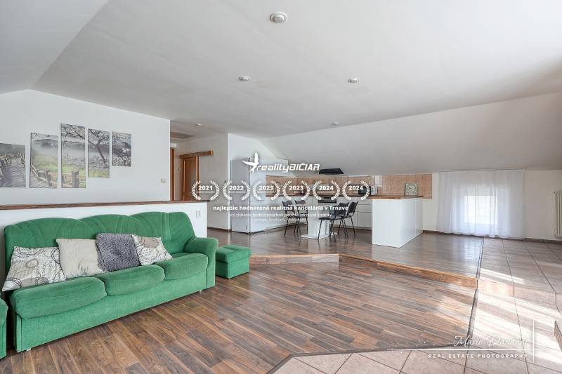 Interiér rodinného domu s pohovkou, kuchyňským koutem a podlahou s dřevěným dekorem.