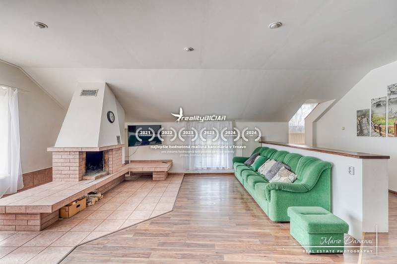 Obývací pokoj v rodinném domě s krbem, zelenou sedačkou a podlahou s dřevěným dekorem.