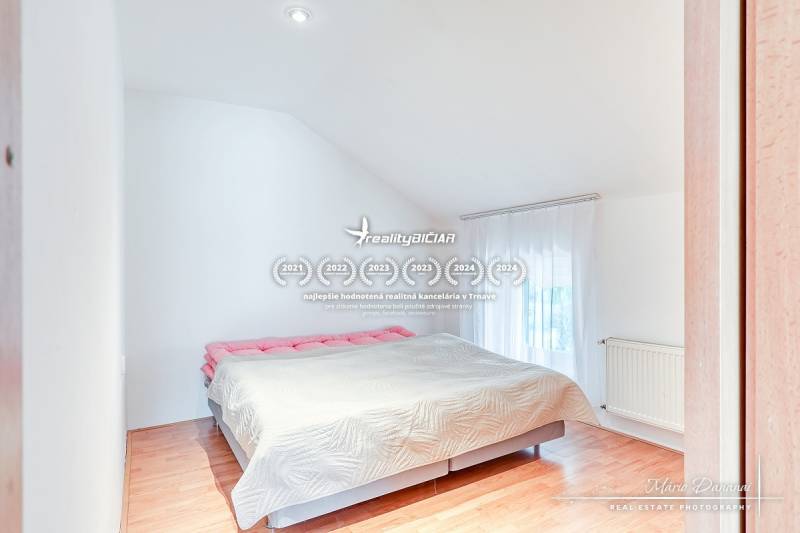 Ložnice v rodinném domě s velkou postelí a podlahou s dřevěným dekorem.