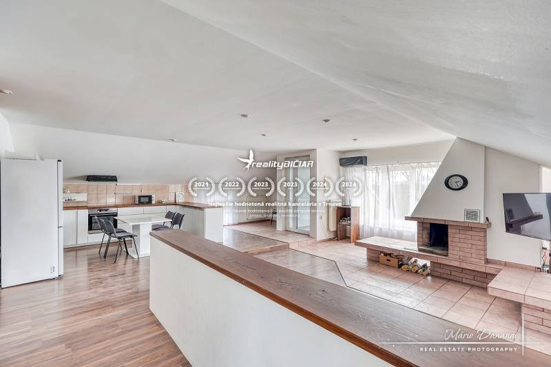 Obývací pokoj s krbem a kuchyňskou částí, podlaha s dřevěným dekorem, světlá místnost.