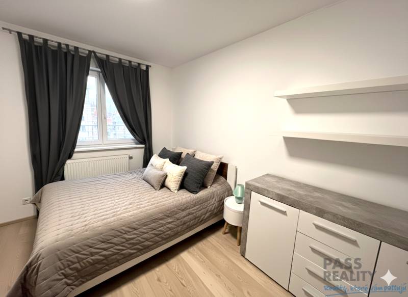 Ložnice v 2-pokojovém bytě s postelí, komodou a závěsy, podlaha s dřevěným dekorem.