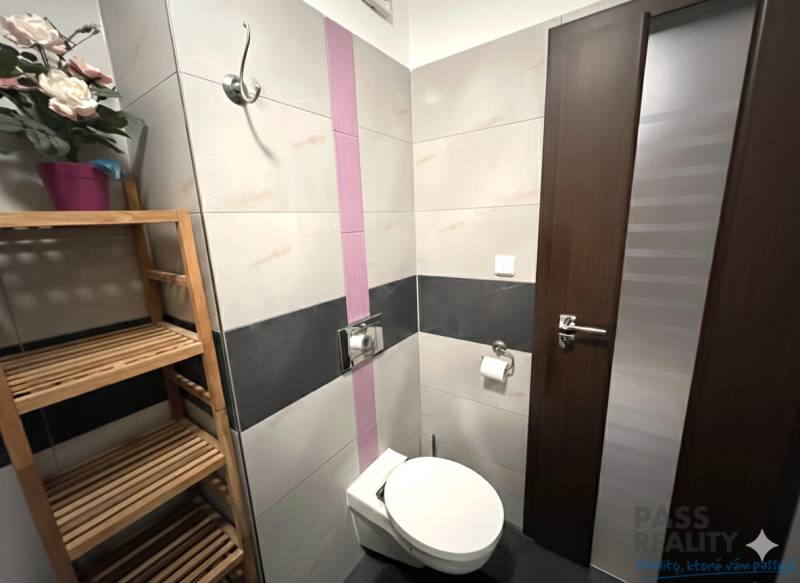 Koupelna v 2-pokojovém bytě s toaletou, dřevěným regálem a dekorativními květinami.