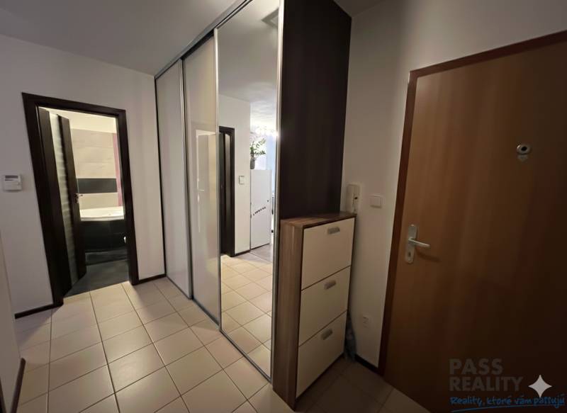 Vstupní hala v 2pokojovém bytě s dlažbou, velkým zrcadlem a skříňkami.