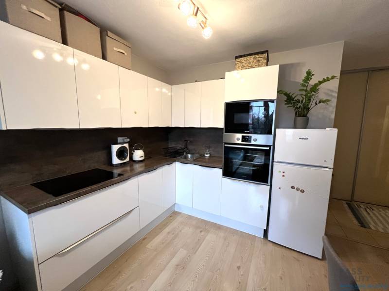 Kuchyně v 2-pokojovém bytě s bílými skříňkami, spotřebiči a podlahou s dřevěným dekorem.