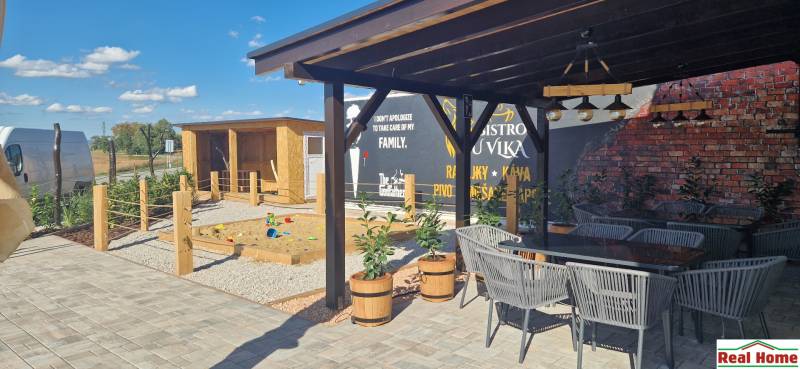 Exteriér v Nové Dedince s gastro prostory, terasou a dětským hřištěm.