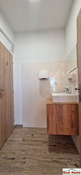 Interiér gastro prostoru se světlými stěnami, podlahou s dřevěným dekorem a umyvadlem.