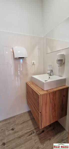 Koupelna s umyvadlem a skříňkou s dřevěným dekorem v gastro prostorech.