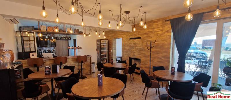 Gastro prostory s visícími světly, dřevěným dekorem a útulným sezením.