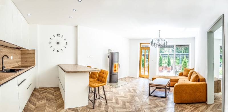 Světlý rekreační apartmán s kuchyní, oranžovou sedačkou a podlahou s dřevěným dekorem.