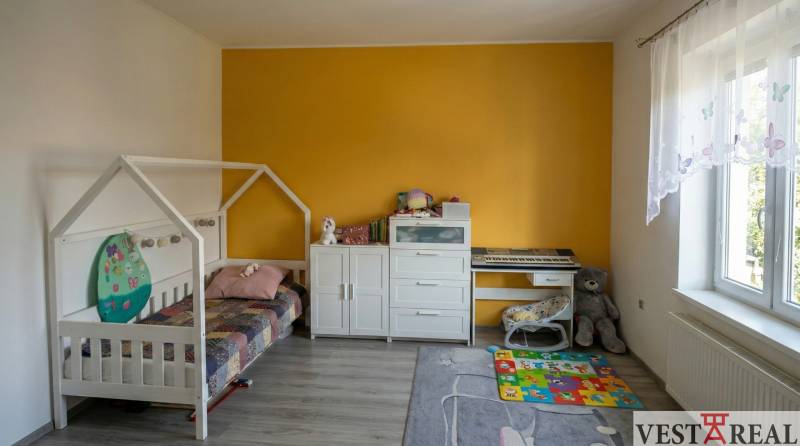 Dětský pokoj s postelí, komodou, klavírem, hračkami a podlahou s dřevěným dekorem ve 2-pokojovém bytě.