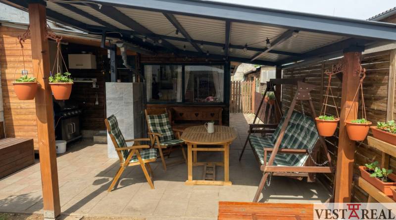 Zahradní posezení s dřevěnými křesly, houpačkou a květináči u 2pokojového bytu.