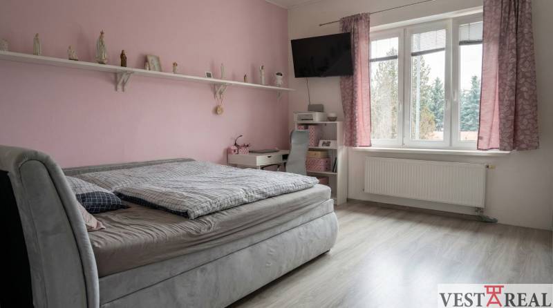 Růžový pokoj s postelí, policemi a podlahou s dřevěným dekorem v 2-pokojovém bytě.