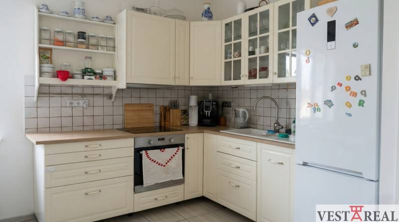 Kuchyně v 2-pokojovém bytě s bílými skříňkami a spotřebiči, podlaha s dřevěným dekorem.