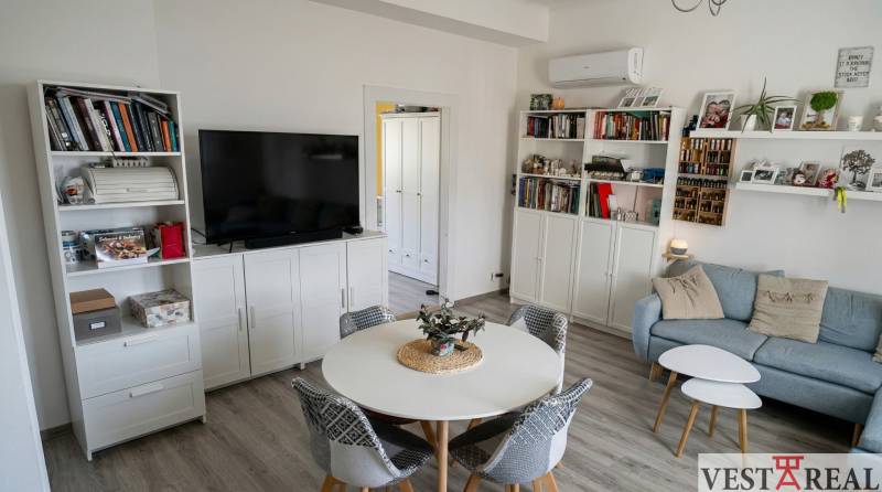 Obývací pokoj v 2pokojovém bytě s podlahou s dřevěným dekorem, gaučem a televizí.