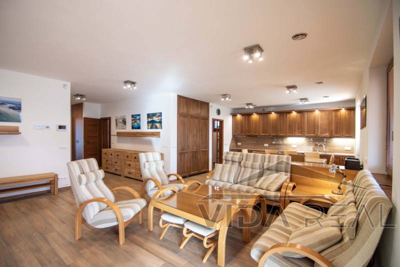 Interiér rodinného domu s prostorným obývacím pokojem, kuchyňskou linkou a podlahou s dřevěným dekorem.