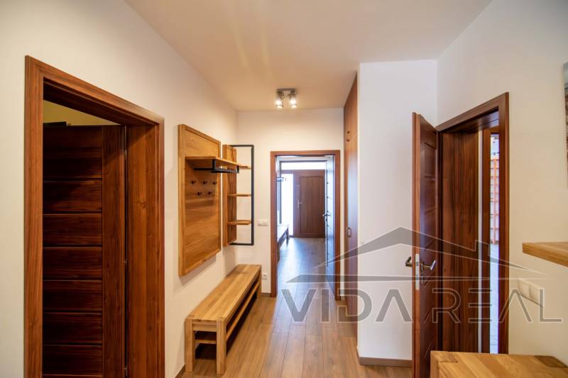 Chodba v rodinném domě s dřevěným dekorem na podlaze a nábytku.