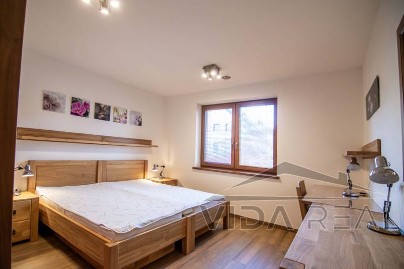 Ložnice v rodinném domě s postelí, nočními lampami a podlahou s dřevěným dekorem.