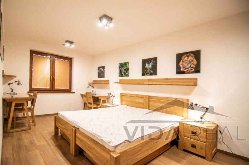 Ložnice v rodinném domě s podlahou s dřevěným dekorem, obrazy a pracovními stoly.