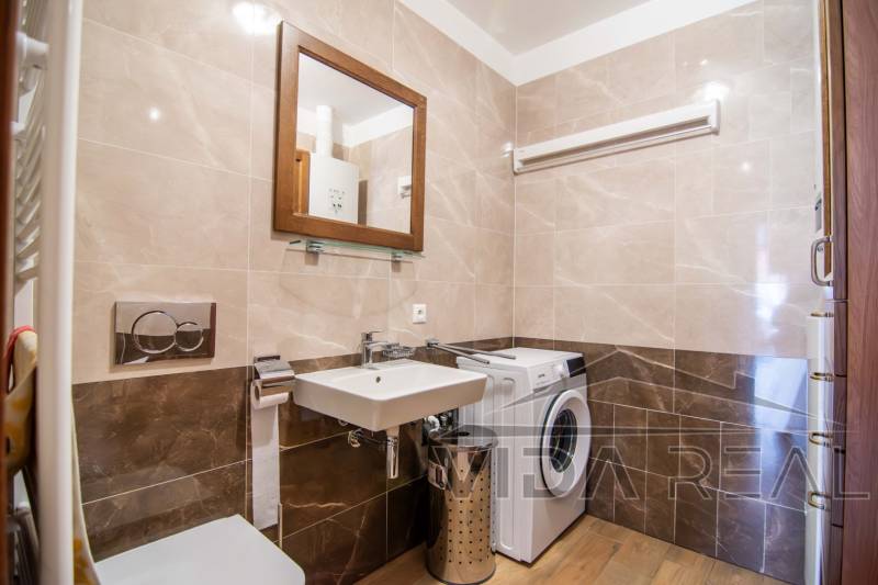 Koupelna v rodinném domě s pračkou, umyvadlem a podlahou s dřevěným dekorem.