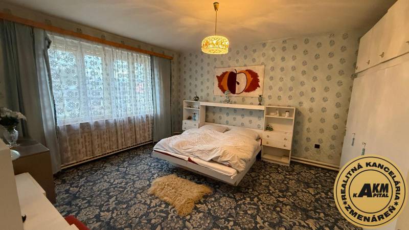 Ložnice v rodinném domě s květinovým kobercem a velkým oknem.