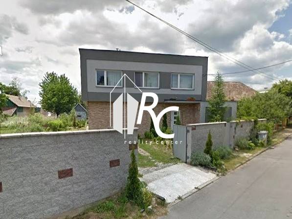 Rodinný dům v Bystričce s upravenou zahradou a vysokým plotem podél ulice.