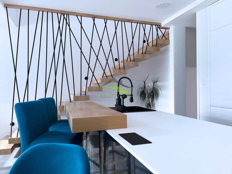 Interiér rodinného domu se schodištěm, modrými židlemi a kuchyňským pultem.