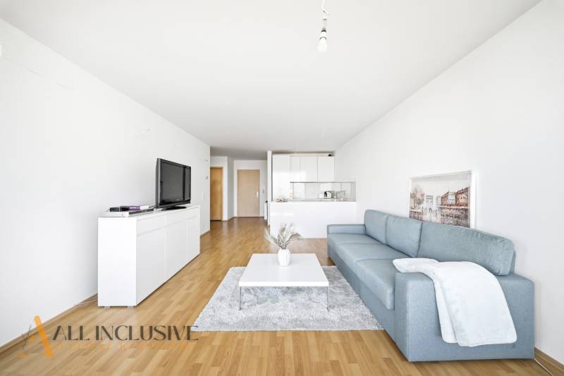 Obývací pokoj s modrou pohovkou, bílým nábytkem a podlahou s dřevěným dekorem ve 2pokojovém bytě.