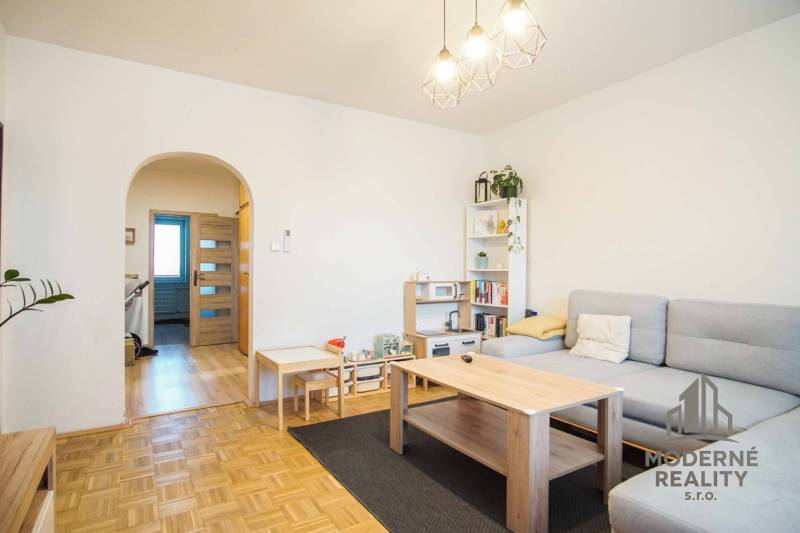 Obývací pokoj v 3-pokojovém bytě s podlahou s dřevěným dekorem a světlým nábytkem.
