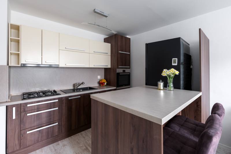 Kuchyně v 2-pokojovém bytě s podlahou s dřevěným dekorem, barovým pultem a moderním vybavením.