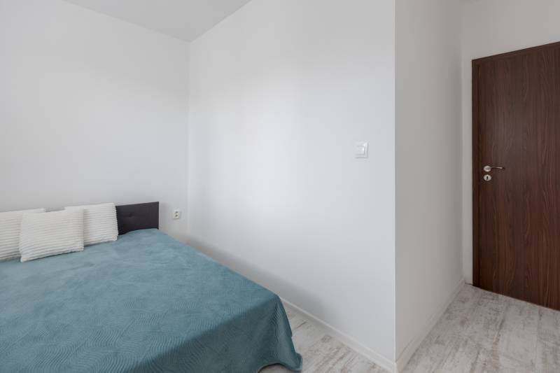 Ložnice v dvoupokojovém bytě s postelí, polštáři a dřevěnými dveřmi.