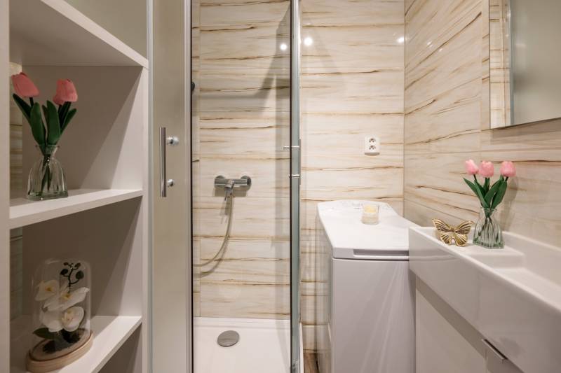 Koupelna s květinami, sprchovým koutem, umyvadlem a zrcadlem v 2-pokojovém bytě.