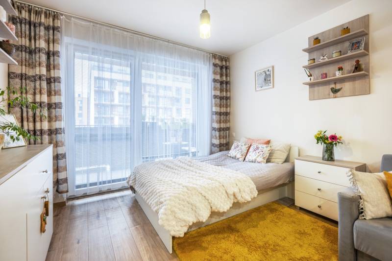 Světlý 1-pokojový byt s postelí, kobercem a podlahou s dřevěným dekorem.