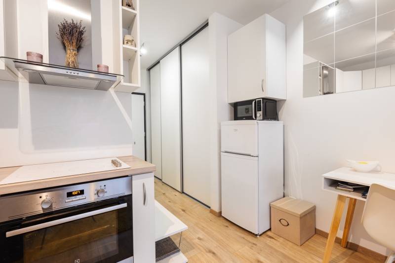 Kompaktní kuchyň s varnou deskou, lednicí a podlahou s dřevěným dekorem v 1-pokojovém bytě.