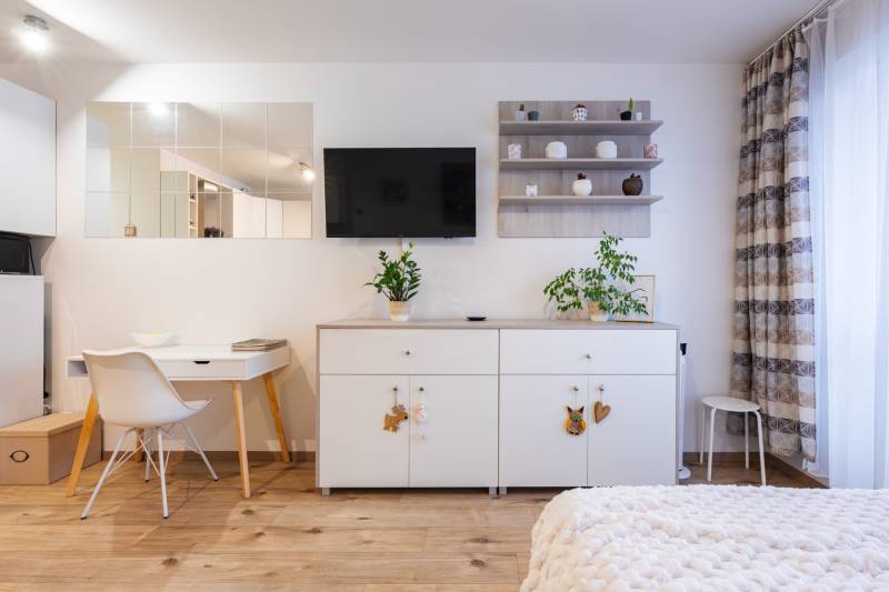 Interiér 1-pokojového bytu s bílým nábytkem a podlahou s dřevěným dekorem.