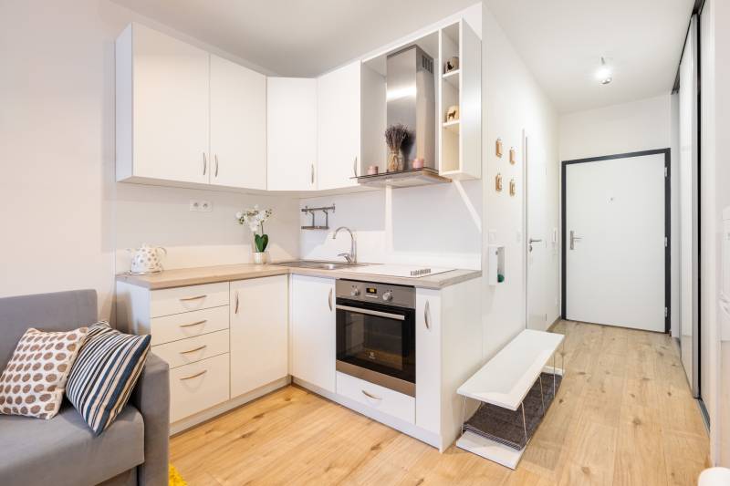 Kuchyně s bílými skříňkami v 1-pokojovém bytě a podlahou s dřevěným dekorem.