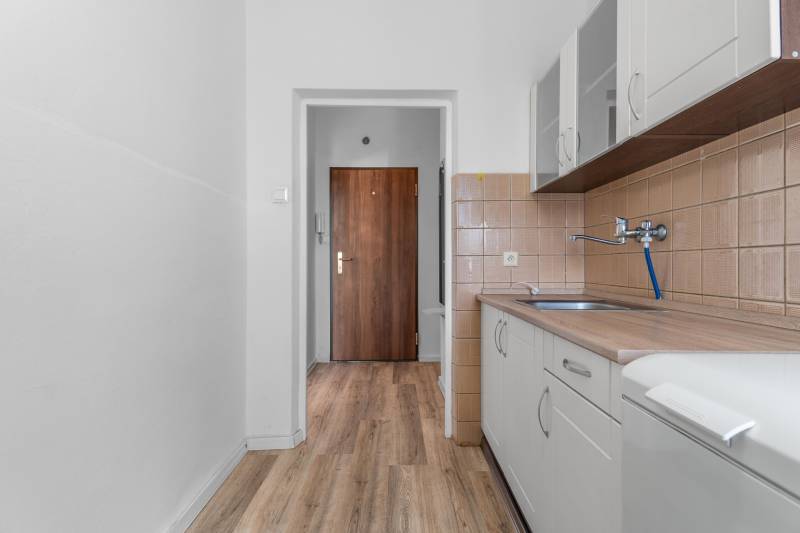 Kuchyňa v 1-izbovom byte s podlahou s dreveným dekorom a bielou linkou.