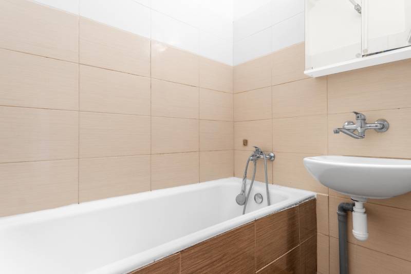 Kúpeľňa s vaňou a umývadlom v 1-izbovom byte, béžová dlažba.