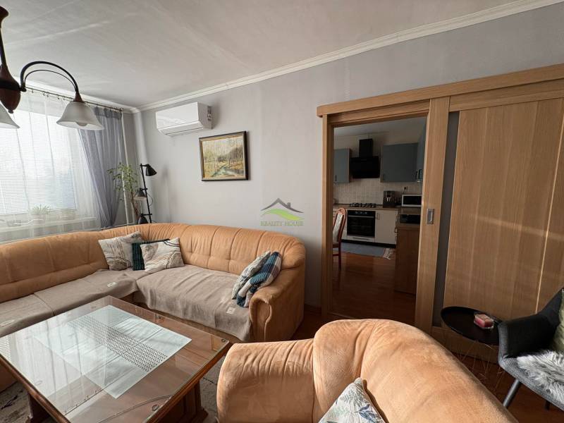 Obývací pokoj s pohovkou, skleněným stolem a kuchyní ve 3pokojovém bytě.